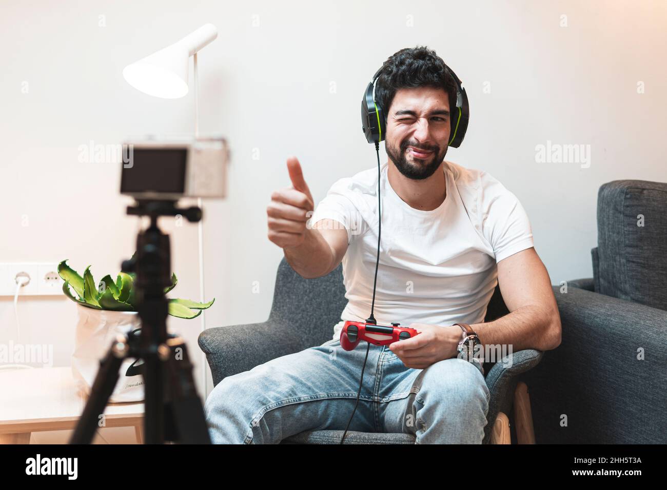 Il giocatore che si inzia e mostra i pollici fino alla fotocamera a casa Foto Stock