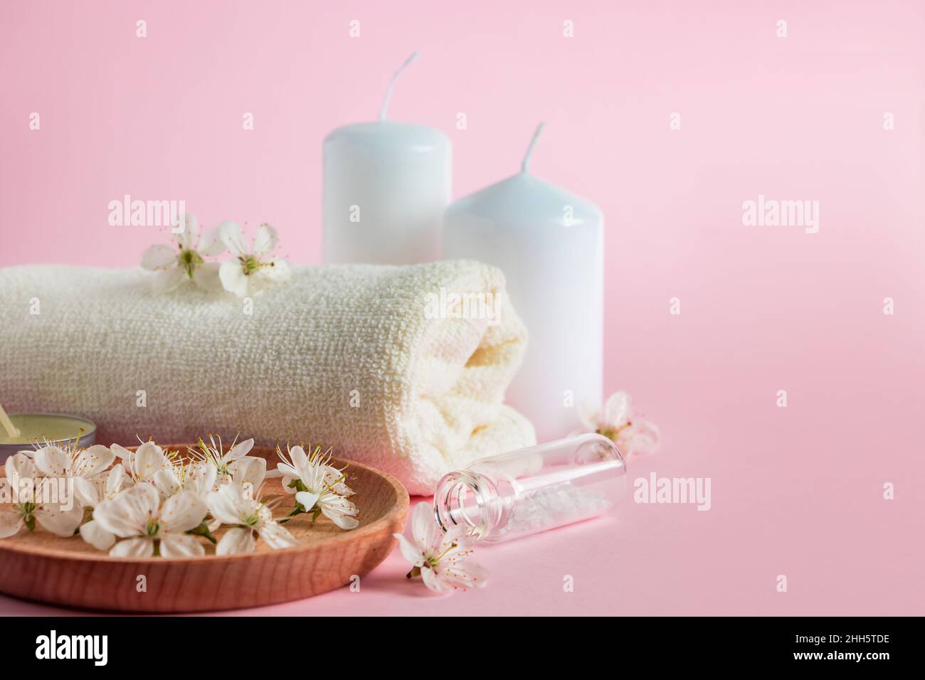 Prodotti cosmetici per spa e aromaterapia. Candele, sale marino, asciugamano e fiori su sfondo rosa. Cura della pelle e concetto di bellezza. Luogo per il vostro te Foto Stock