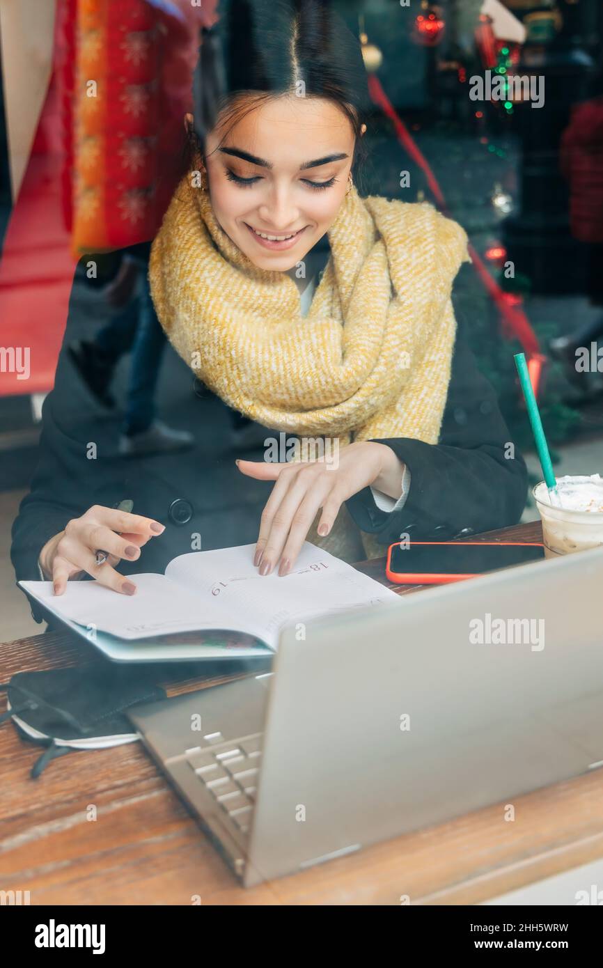 Ragazza sorridente che legge diario visto attraverso un bicchiere di caffè Foto Stock