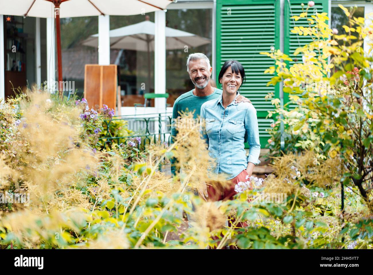 Uomo felice braccio intorno alla donna in mezzo a piante in cortile Foto Stock
