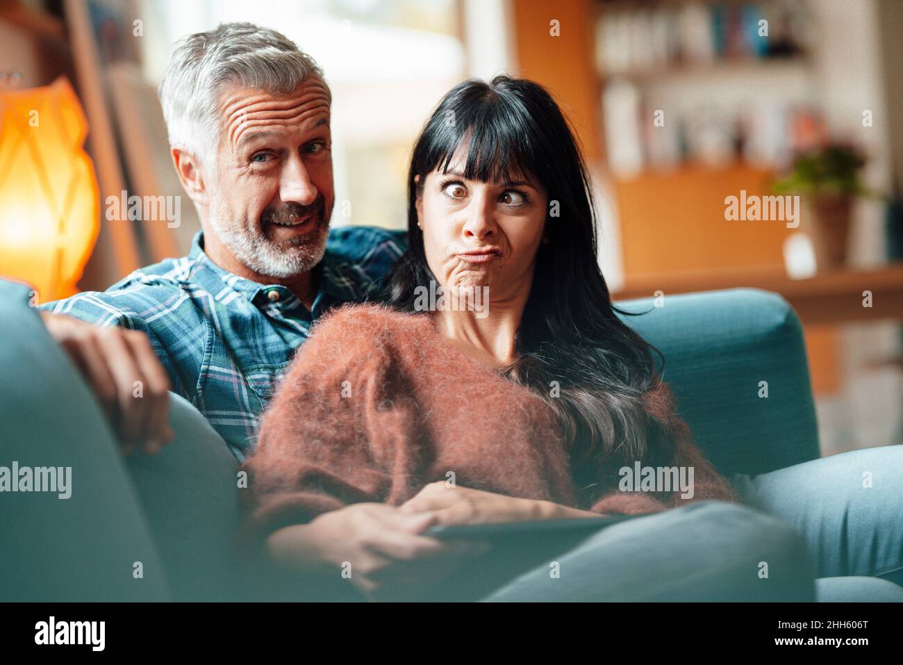 Donna che fa faccia divertente da uomo in salotto Foto Stock