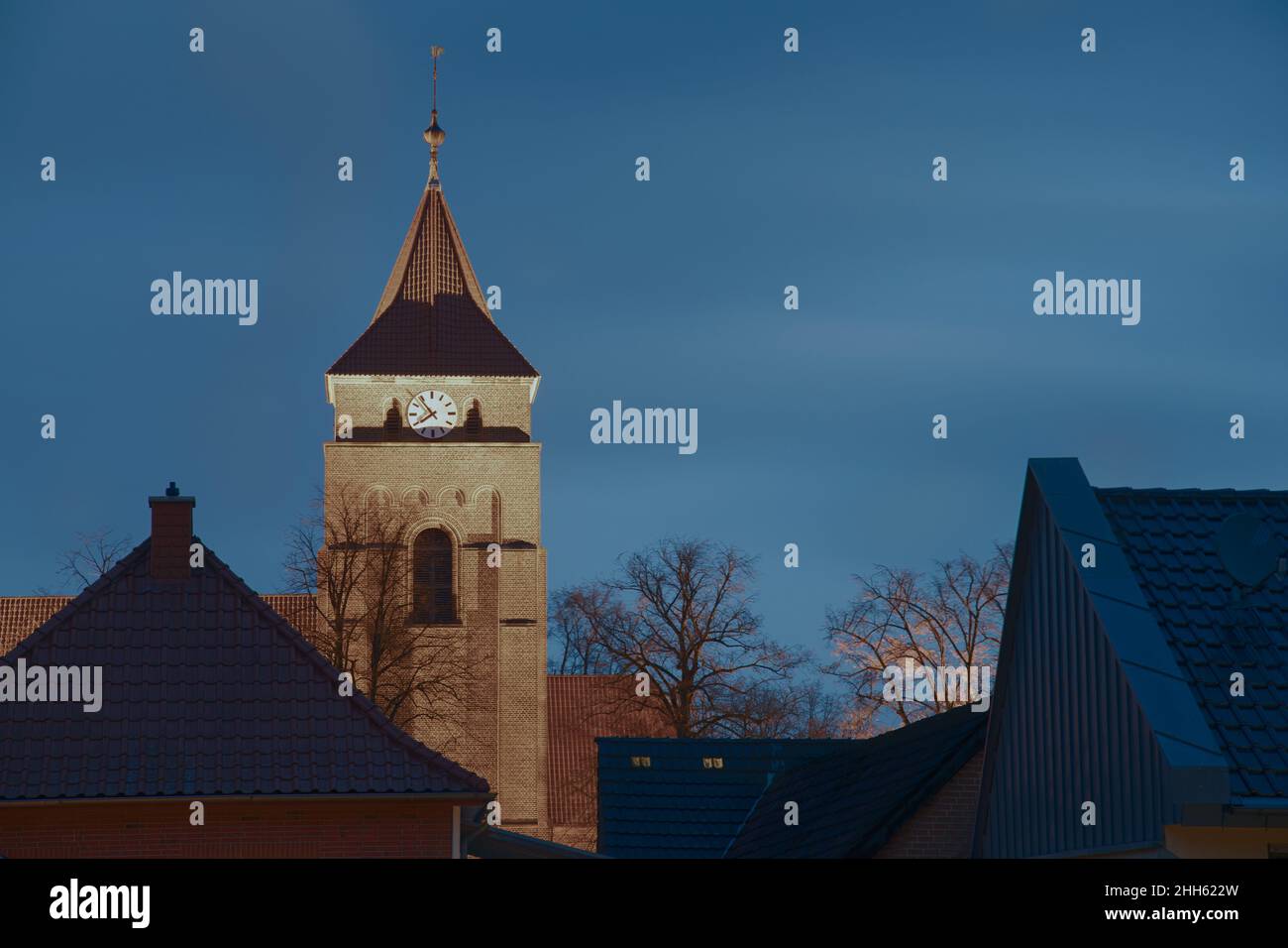 Villaggio chiesa torre illuminata in inverno con un orologio all'ora blu Foto Stock