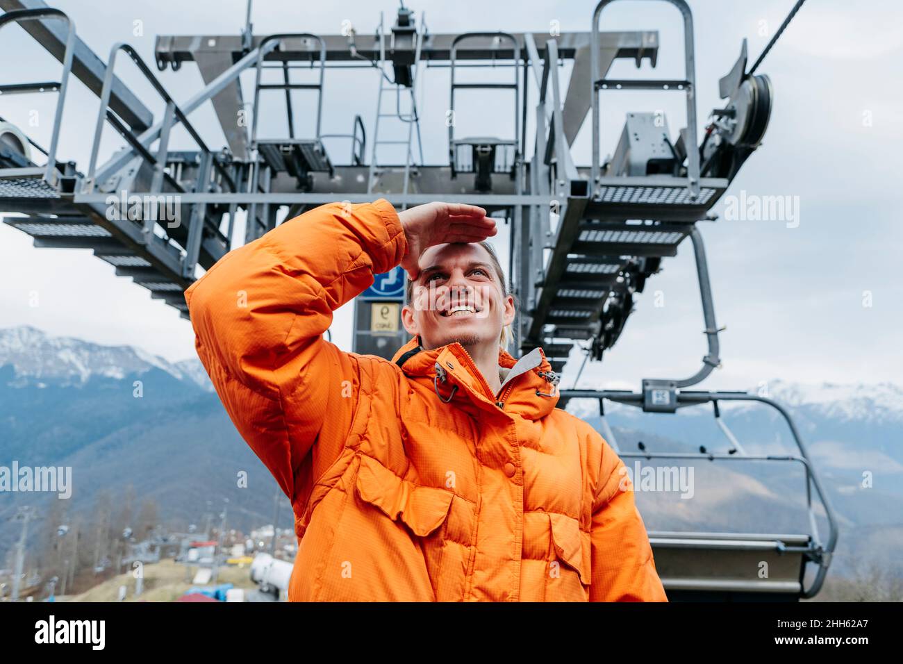 Uomo felice in giacca arancione occhi di schermatura alla stazione della funivia Foto Stock