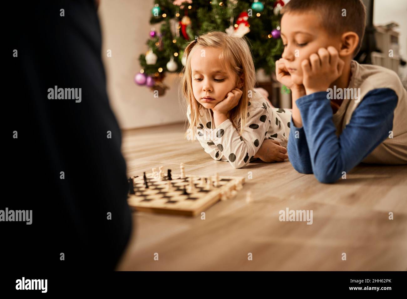 Ragazzo e ragazza sdraiati sul pavimento guardando la scacchiera a casa Foto Stock