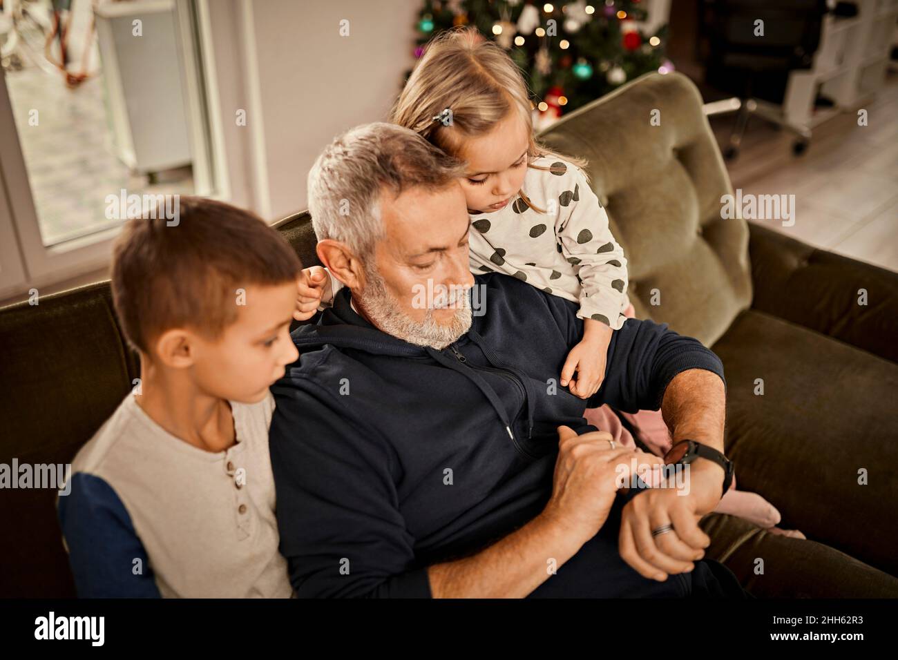 Nonno che insegna i controlli di smart watch ai nipoti seduti sul divano a casa Foto Stock