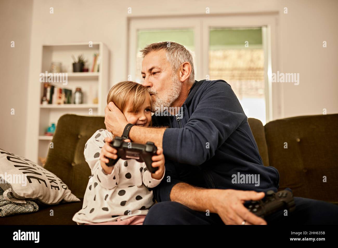 Nonno bacia la nipote tenendo il joystick a casa Foto Stock