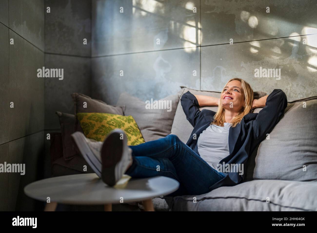 Donna d'affari che si rilassa con le mani dietro la testa sul divano in ufficio Foto Stock