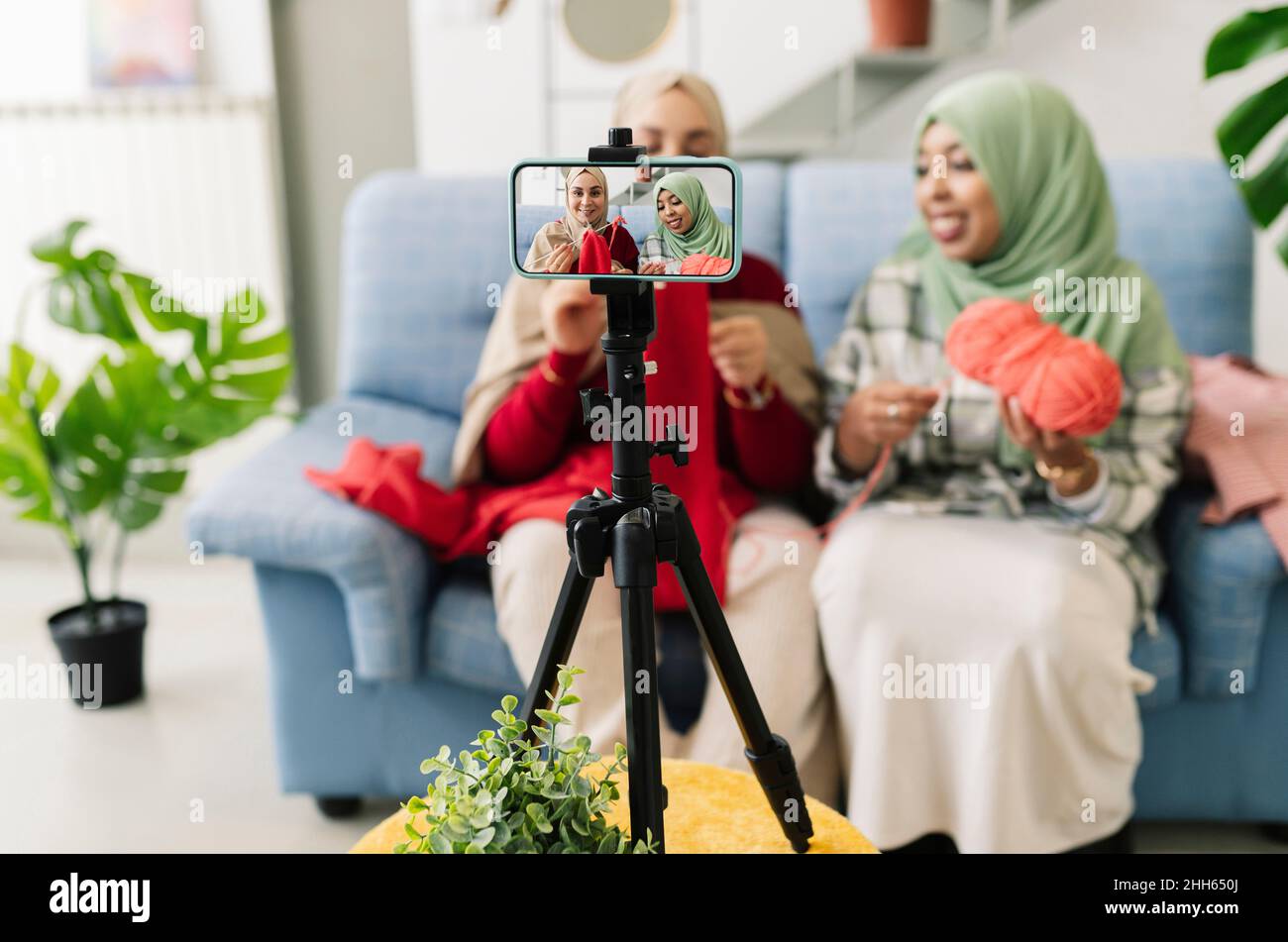 Amici che creano vlog di lavoro a maglia su smartphone a casa Foto Stock