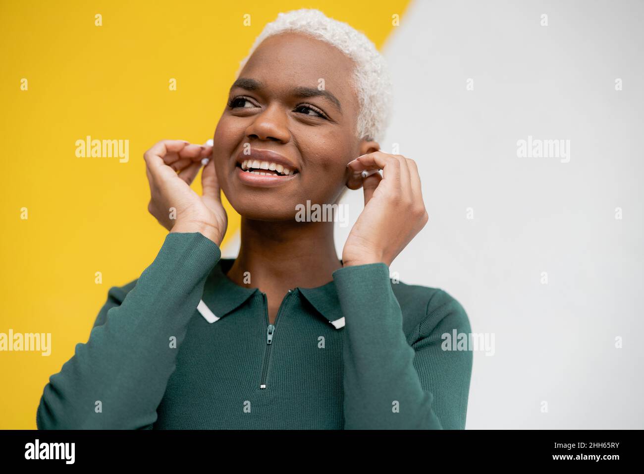 Donna sorridente che indossa cuffie intrauricolari davanti alla parete Foto Stock