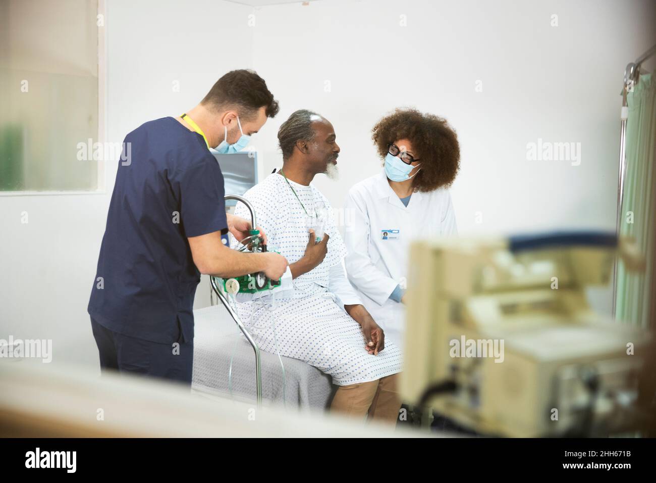 Infermiera con macchina per ossigeno da parte del paziente che parla con il medico in sala medica Foto Stock