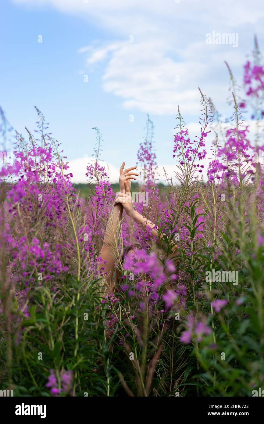 Donna con gesture alzata a mano in mezzo a piante fiorite rosa Foto Stock