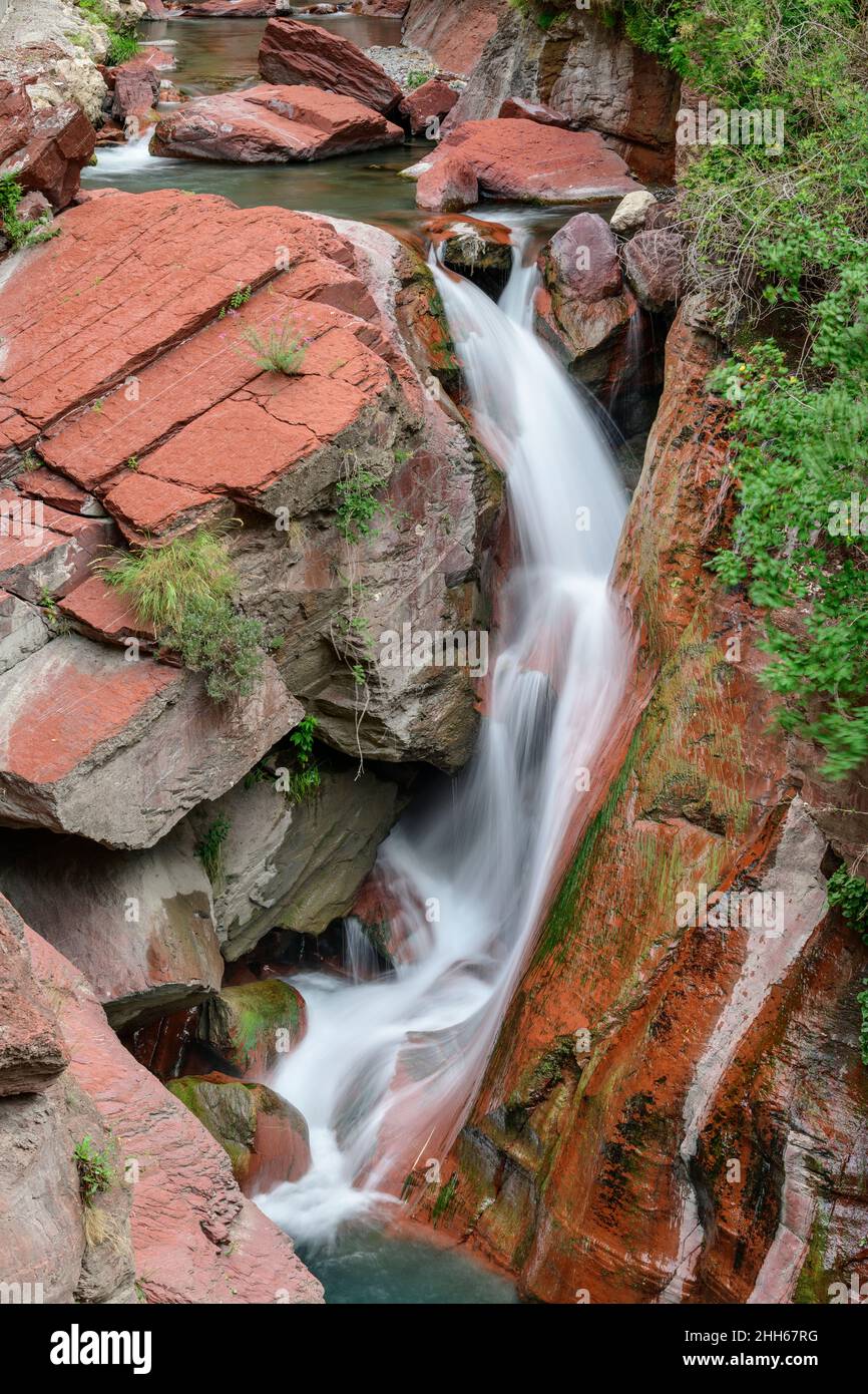 Cascata che scorre tra le Alpi Marittime rosse, Parco Nazionale del Mercantour, Francia Foto Stock