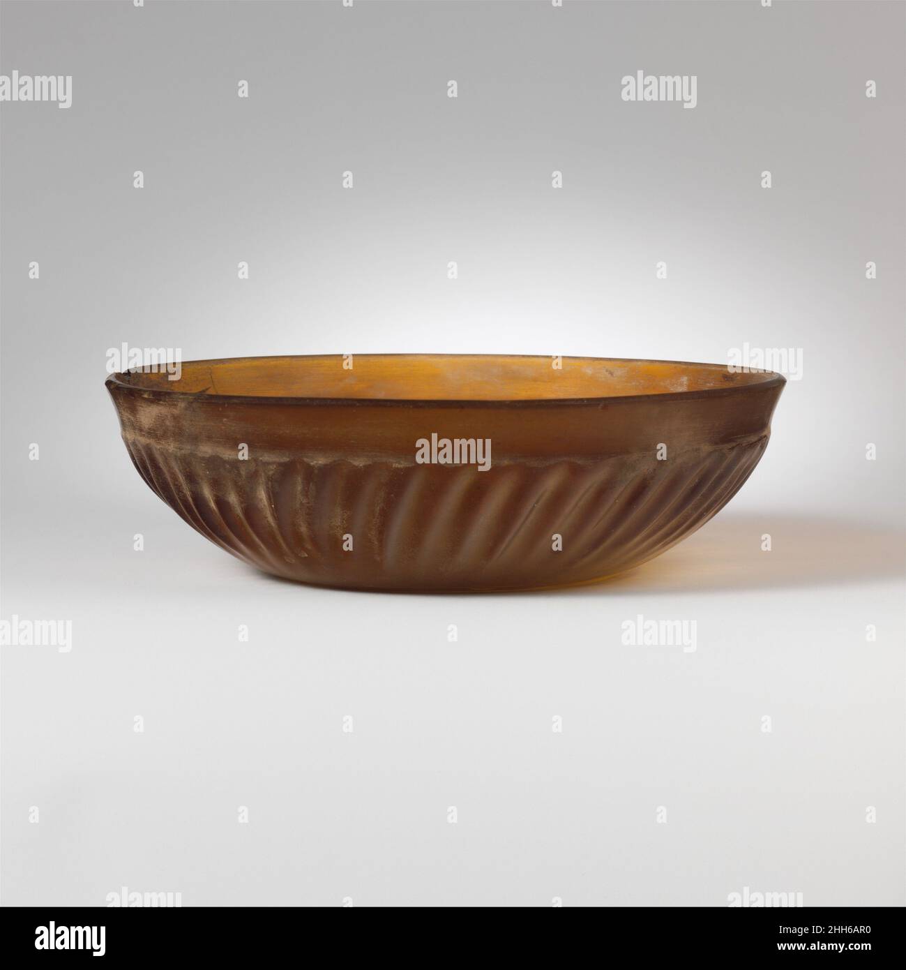 Vaso in vetro costato fine 1st secolo a.C.–metà 1st secolo d.C. Romano traslucido miele marrone.bordo estricato, con bordo quasi appuntito e banda concava inclinata verso l'interno; lato curvato verso il basso; fondo concavo.su interno, sottile scanalatura orizzontale sul bordo interno del bordo, due scanalature concentriche intorno al fondo e piccolo cerchio più largo al centro; Sull'esterno, cinquantuno nervature leggermente inclinate di lunghezza e larghezza variabili, con le cime smerigliate, disposte intorno alla sezione centrale in rilievo di body.intact, tranne una piccola scheggiatura e spaccatura nel bordo; alcune crepe interne di deformazione; poche bolle; dulling su interi Foto Stock
