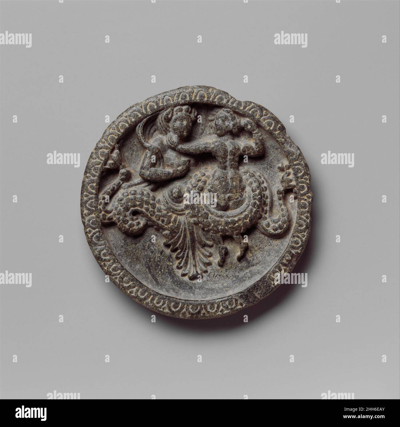 Piatto con creatura marina e coppia 1st secolo a.C. Pakistan (antica regione di Gandhara) questo piatto della regione antica di Gandhara risale al secondo secolo a.C. al primo secolo d.C. Commercio internazionale con il mondo ellenistico e l'India, nonché invasioni in Gandhara da parte degli Scithians, Parthians e Kushans hanno portato molti nuovi idiomi stilistici che hanno modellato il vocabolario stilistico di questi oggetti. Piatti simili sono stati trovati nella città Gandharan di Sirkap (Taxila) in contesti che suggeriscono che sono stati utilizzati per rituali domestici, forse per garantire un'aldilà positiva. Piatto con Foto Stock