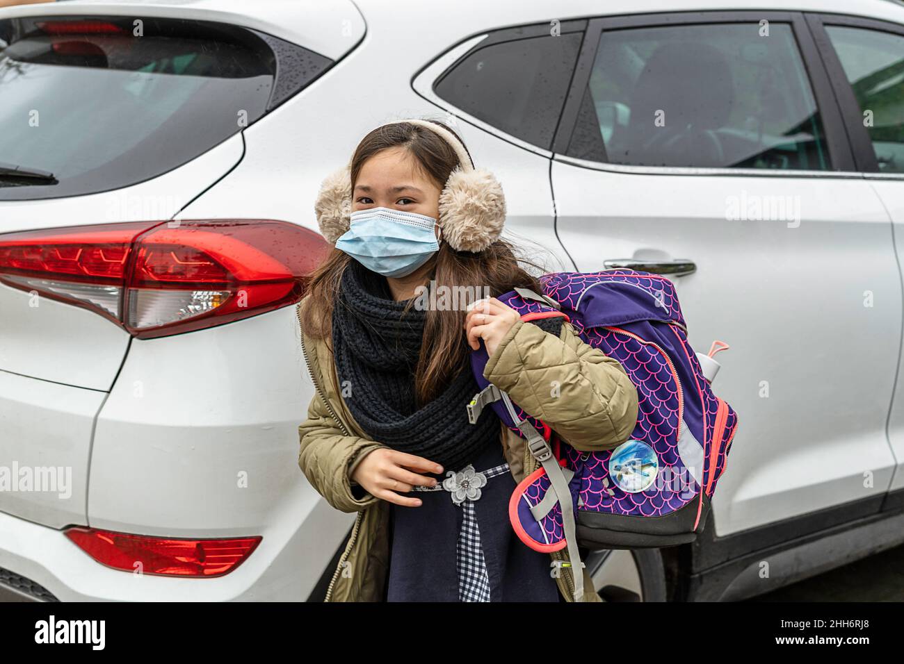 La ragazza giovane è portata a scuola da car.Young ragazza con la borsa a mano sulla parte posteriore esce dall'automobile Foto Stock