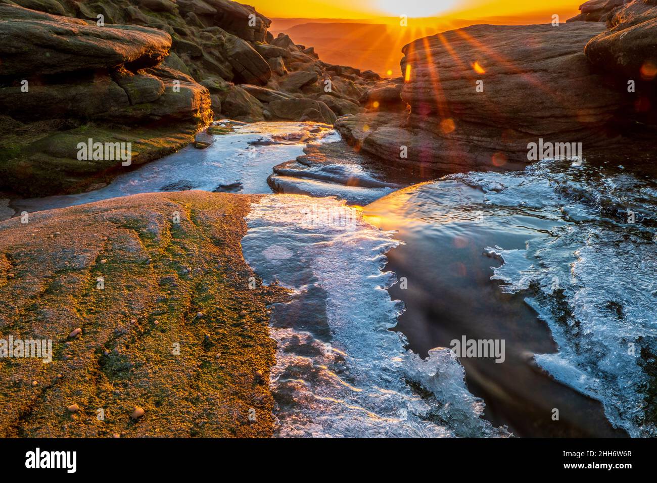 Ghiaccio sul fiume Kinder a Kinder Downfall nel Peak District, prendendo il sole in lontananza Foto Stock