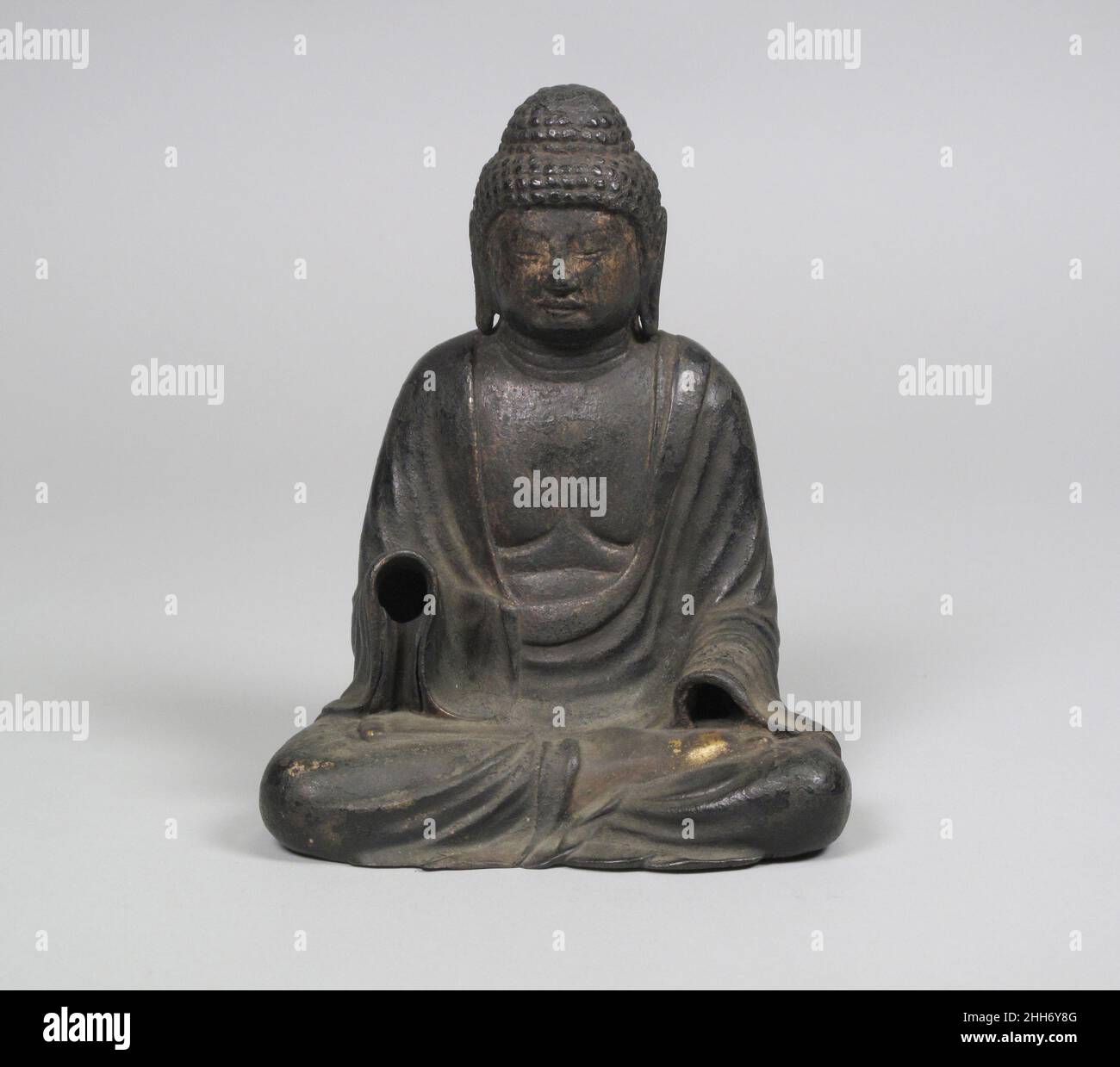 Buddha seduto 10th–11th secolo Giappone questa piccola immagine rappresenta probabilmente Shakyamuni, lo storico Buddha, nel suo stato illuminato, seduto nella postura della meditazione. Corti coralli di capelli (rahotsu) coprono la testa, e una protuberanza cranica simboleggia la sua profonda saggezza. Le mani, che furono gettate separatamente, avrebbero formato i caratteristici mudri associati alla sua immagine: La destra, sollevata e aperta in un gesto di rassicurazione, rappresenta il dono benevolo della vita senza paura che è il risultato dell'illuminazione buddista; la sinistra, appoggiata sul ginocchio con il palmo aperto, si estendeva a. Foto Stock