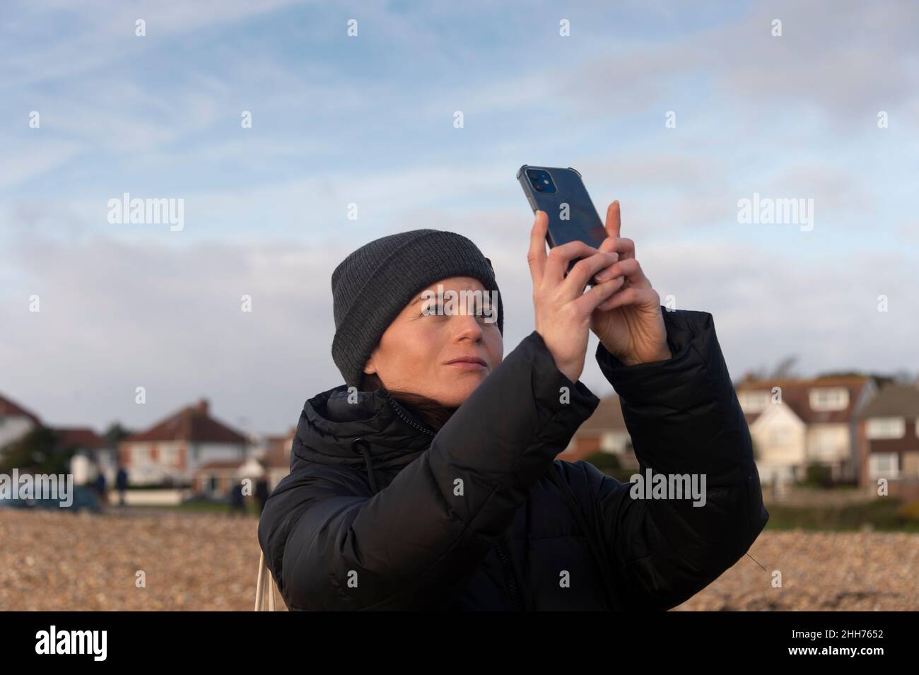 Donna che indossa un cappello lanoso che prende un selfie su un telefono cellulare, all'aperto inverno. Foto Stock