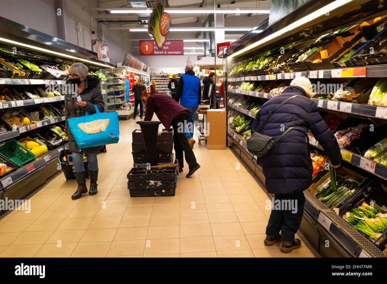 Sainsbury's Supermarket mostra di ben rifornito scaffali di frutta e verdura uomo e donna shopping e una donna assistente scaffali impilamento Foto Stock