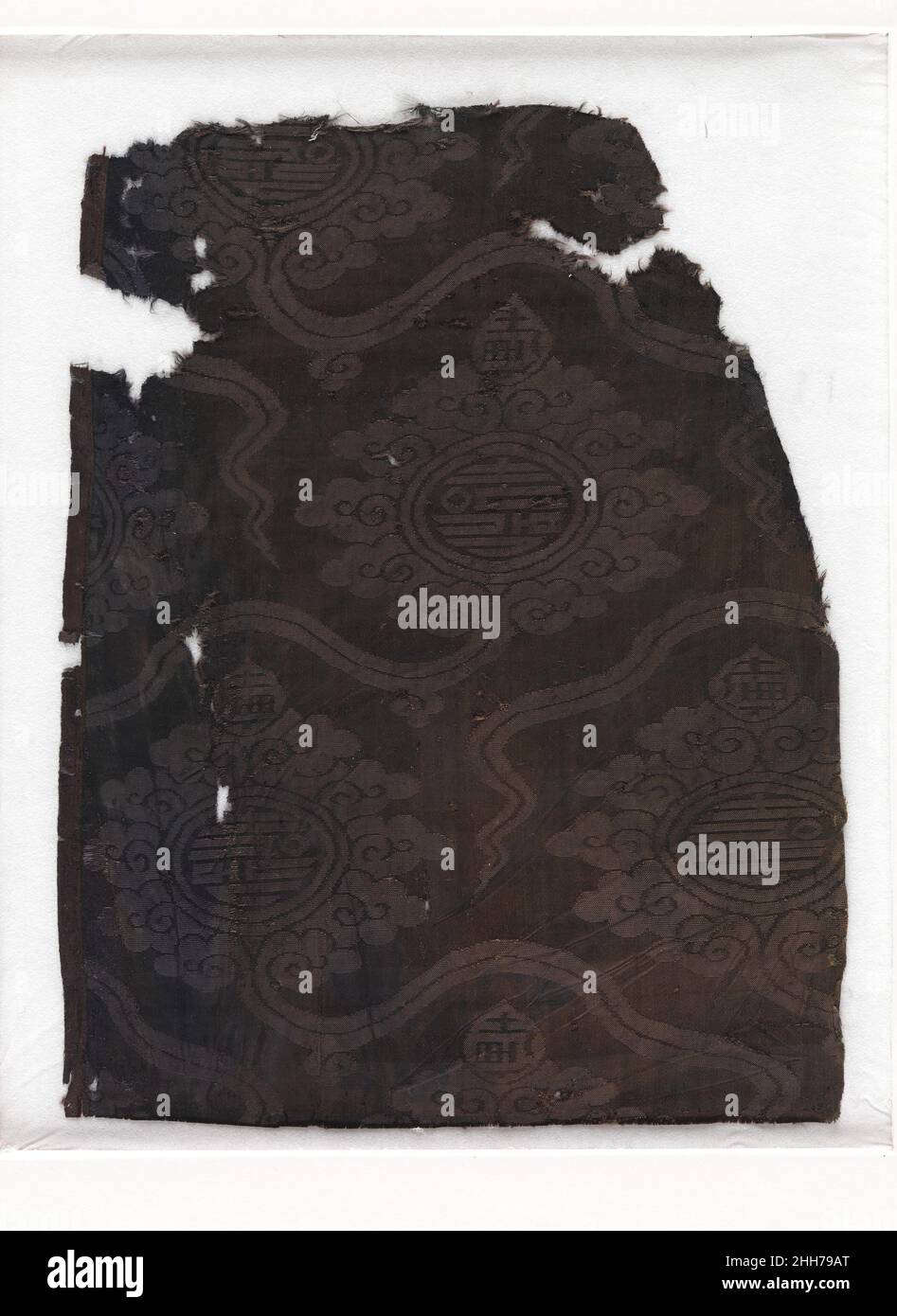 Damask with Cloud Palmette and Chinese characters 14th Century Cina il commercio o la diplomazia devono aver giocato un ruolo nella vita dei tessuti come questo esempio (ora oscurato ma originariamente blu), che, secondo i dati, è stato trovato in Egitto. Il modello palmette ha avuto origine nell'Asia centrale e nel mondo iraniano orientale. Qui, presenta anche un bordo della nuvola cinese e versioni perfette del carattere cinese per longevità (shou) al centro e in cima a ciascuno. Le damasche longevità come questo pezzo devono essere state presenti anche in altre regioni, in quanto probabilmente hanno ispirato i disegni Foto Stock