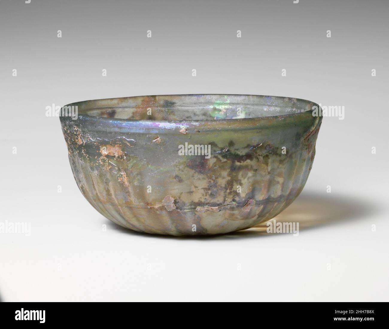Coppa con nervature di vetro fine 1st secolo a.C.–inizio 1st secolo d.C. romana traslucido blu pallido verde.bordo arrotondato verticale; lati profondi con nastro liscio intorno alla parte superiore, curvando verso il basso leggermente concavo.su interno, un'ampia scanalatura orizzontale sotto il bordo, e due scanalature strette e ravvicinate tagliate in una fascia intorno al corpo inferiore; Sull'esterno, trentotto costole poco profonde e leggermente inclinate, rastremandosi verso il basso ed estendendosi al bordo di bottom. Intatto, ma alcune crepe interne; bolle di pinprick; dulling, vaiolando profondo, e iridescence, Con macchie di agenti atmosferici cremosi spessi.segni di smerigliatura rotativi su interni e su Foto Stock