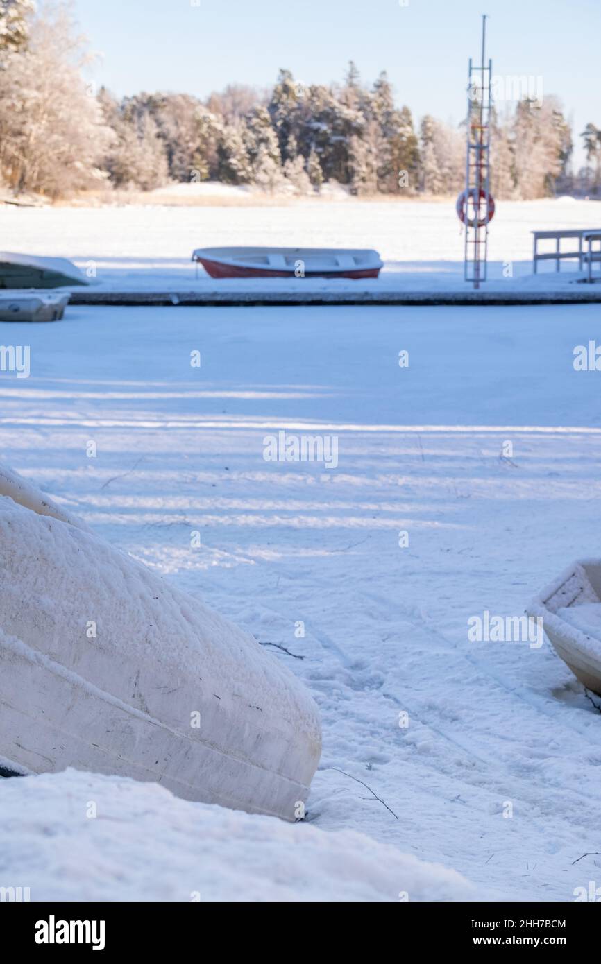 Helsinki / Finlandia - JANUARU 17, 2022: Vista delle barche abbandonate in fila sulla riva con il sole invernale che illumina lo sfondo. Foto Stock