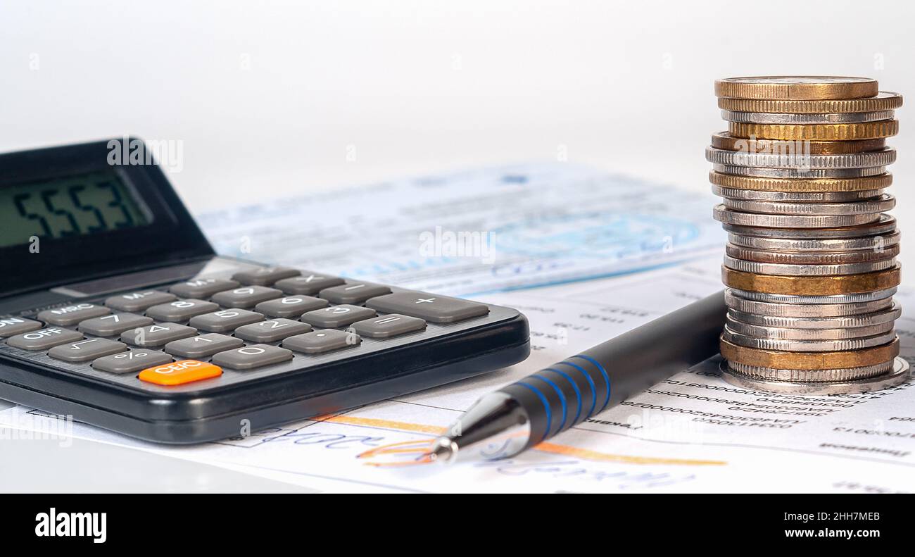 Collumn di monete su sfondo di fatture e assegni, calcolatrice e penna. Concetto finanziario e bancario, finanze domestiche Foto Stock