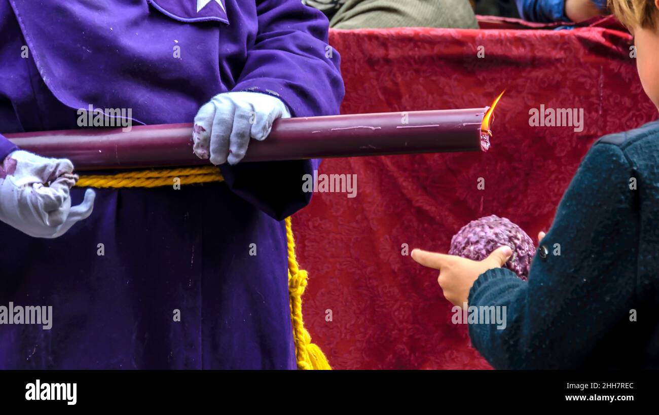 Un ragazzo fa una palla di cera, sgocciolando da una candela in una processione della settimana Santa a Huelva, Spagna Foto Stock