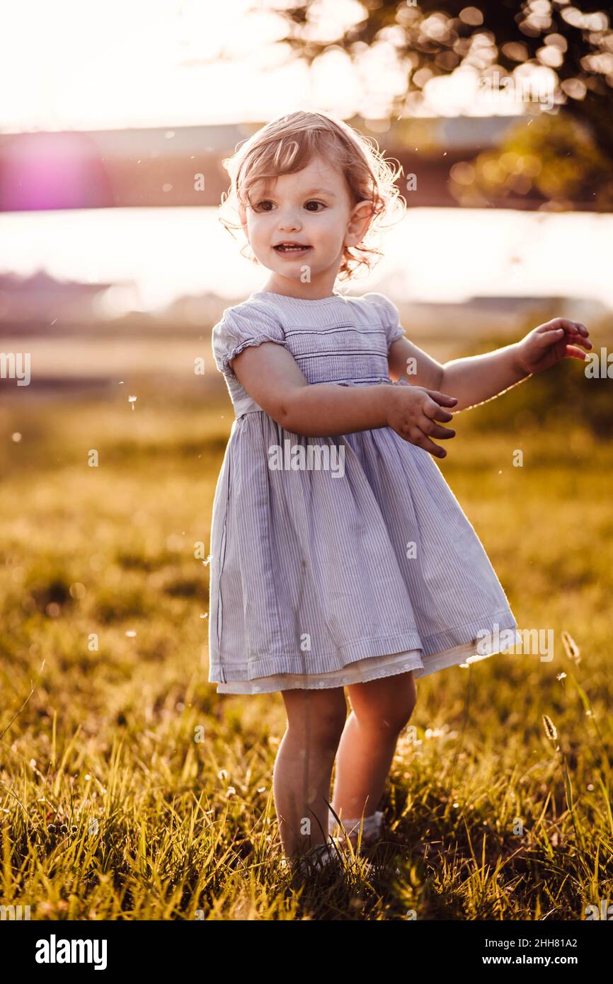 Carino, bambina in abito bianco guardando qualcosa. Luce pomeridiana Foto Stock