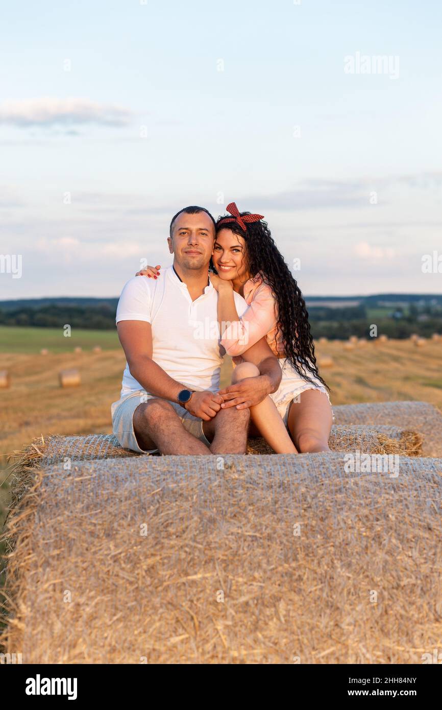 Coppia amorevole in un campo su rotoli di paglia. Giovane uomo e donna che si divertono, abbracciano e baciano al tramonto. Foto Stock