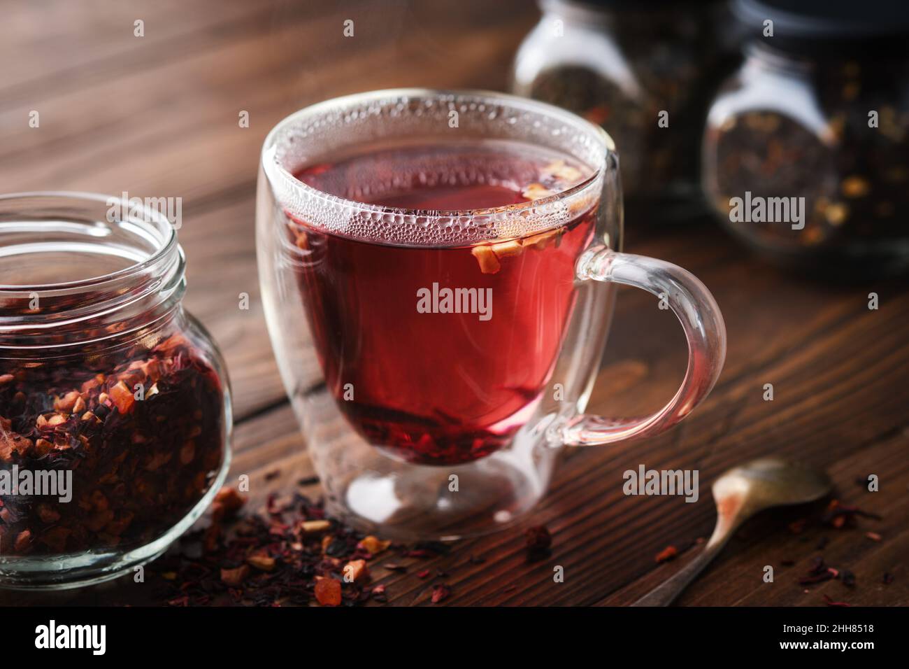 Bicchiere di tè caldo aromatico alla frutta rossa, vasetto di tè naturale alla frutta con petali di ibisco, fette di frutta e bacche. Vasetti di tè alla frutta aromatica sul dorso Foto Stock