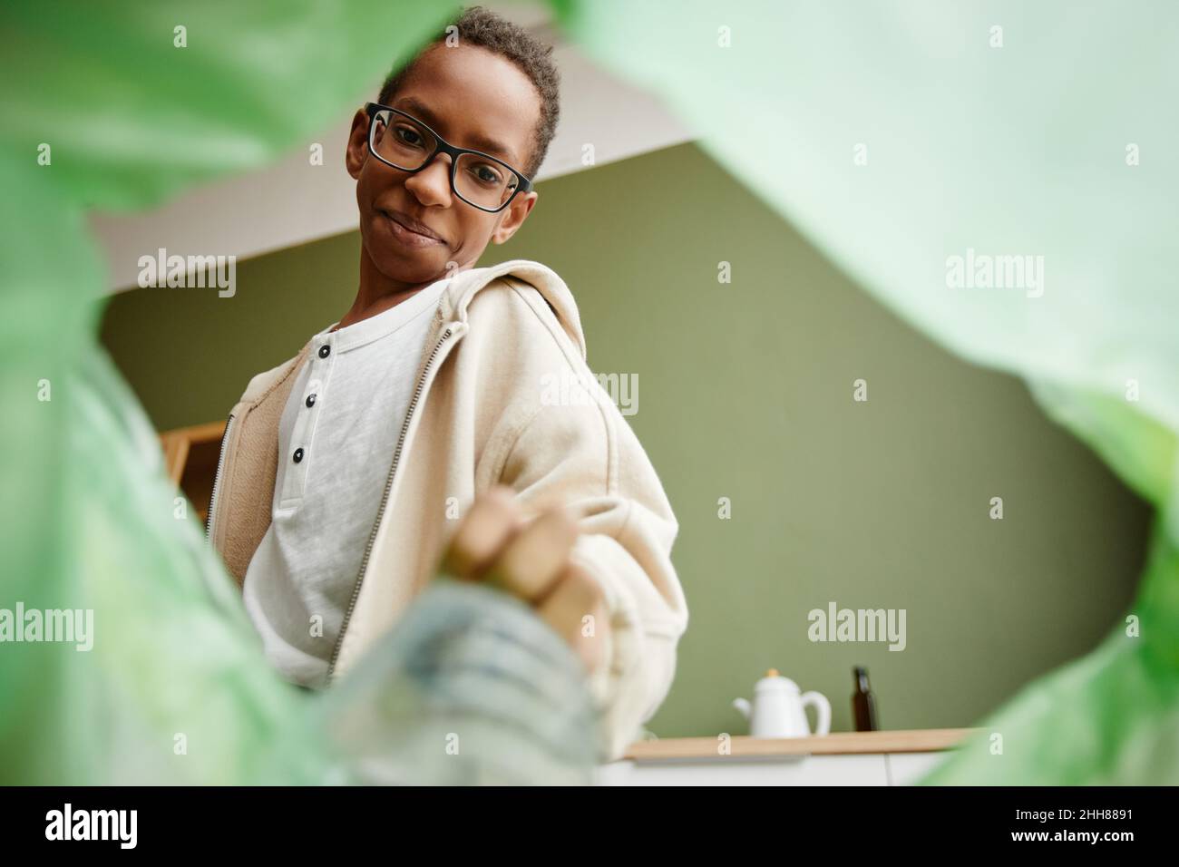 Vista ad angolo basso presso il ragazzo afroamericano smistamento rifiuti domestici a casa, riciclaggio bin POV Foto Stock