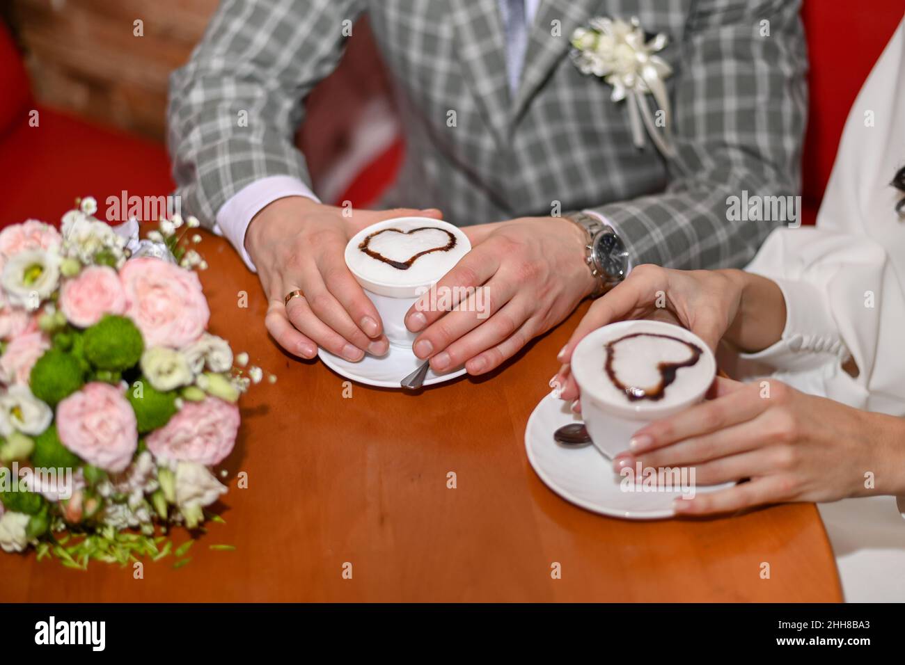 le mani maschili e femminili contengono una tazza di cappuccino con schiuma a forma di cuore. Foto Stock