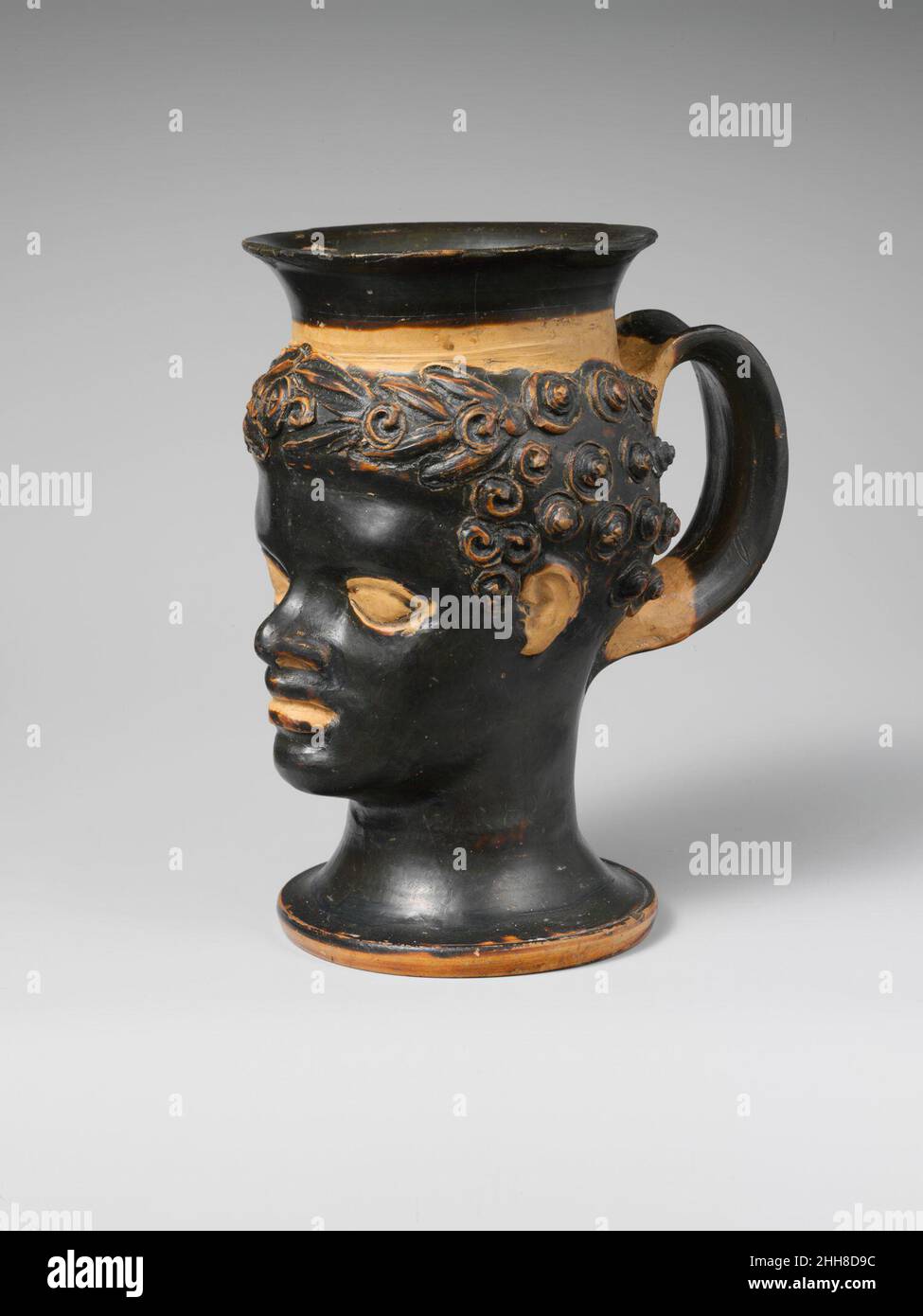 Tazza di terracotta a forma di testa nera di un ragazzo africano fine 4th secolo a.C. Etrusca questo ragazzo indossa una corona di foglie d'oliva decorata con un medaglione centrale. Tazza di terracotta a forma di testa nera del ragazzo africano 254849 etrusca, tazza di terracotta a forma di testa nera del ragazzo africano, fine 4th secolo a.C., Terracotta, H. 6 pollici. (15,2 cm). Il Metropolitan Museum of Art, New York. Dono di El Conde de Lagunillas, 1956 (56.49.2) Foto Stock