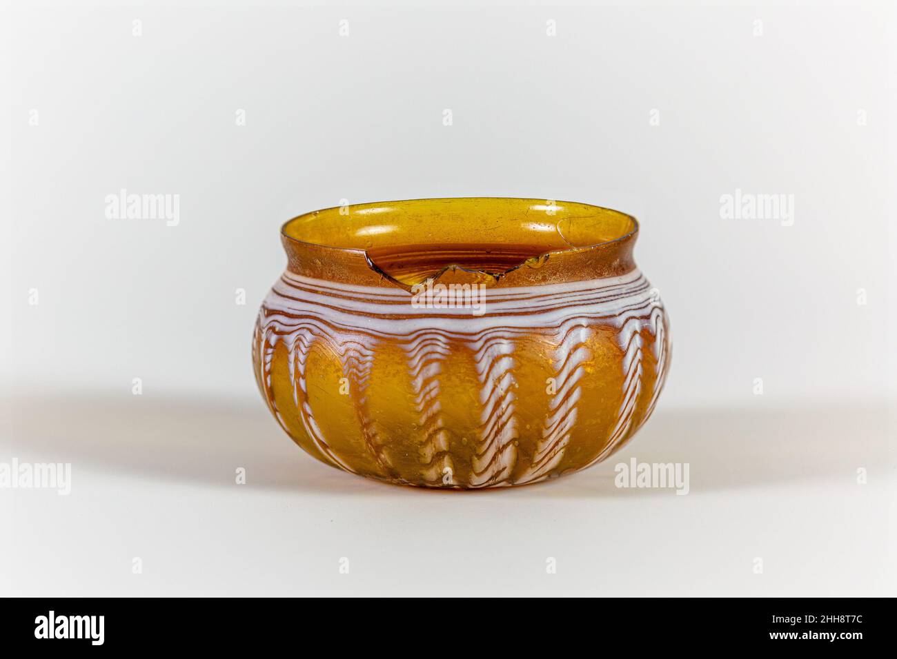 Bicchierino con nervature di vetro metà 1st secolo d.C. Roman traslucido miele marrone; prova in bianco opaco.Knocked-off, bordo smerigliato; collo concavo corto; corpo globulare squat curvato in fondo largo, spesso, piatto.Trail avvolto a spirale dal fondo intorno al corpo, con un'ampia zona in lato tra le nervature; Lati utensili in diciotto, poco profondo, irregolare, verticale ribs.Complete, tranne che per grande chip nel bordo; alcune bolle; dulling, iiridescence debole, intemperie di traccia tra costole, e una patch di cremoso marrone intemperie su interno.. Ciotola in vetro con nervature. Romana. Metà del 1st secolo d.C.. Vetro; soffiato, trainato, e toole Foto Stock