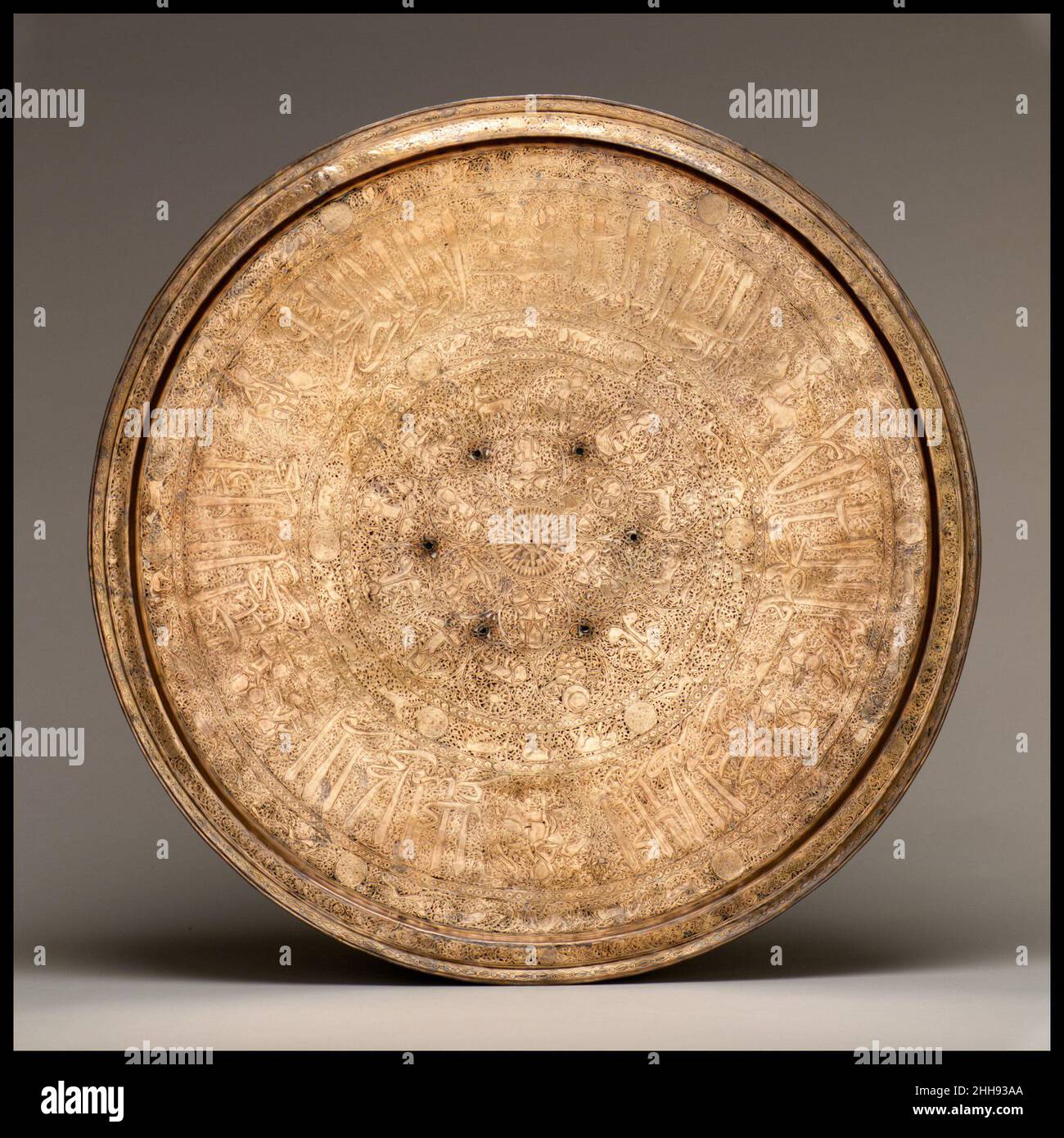 Vassoio fine 13th–inizio 14th secolo questo vassoio ha fasce concentriche di decorazione intorno ad un disco centrale del Sole. Sono incluse nelle band le personificazioni dei sei pianeti e i dodici segni dello zodiaco, gli animali cortesi, e un'iscrizione (i titoli di un ufficiale Mamluk) con medaglioni contenenti un falconer, giocatori di polo, E musicisti seduti. Nella tradizione araba, la costellazione del Sagittario era conosciuta come al-rami, 'l'arciere', mentre il corrispondente segno zodiaco era conosciuto come al-qaws, 'l'arco.' Di conseguenza, rappresentazioni del segno zodiaco, un centauro che spara una freccia dal suo bo Foto Stock