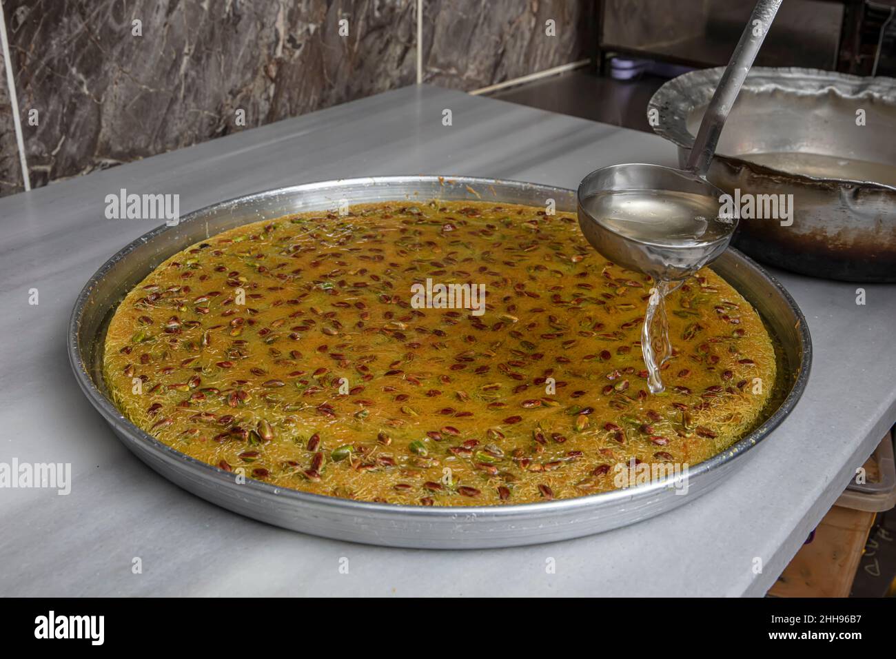 Dessert Kadayif con pistacchio su un vassoio nel laboratorio kadaif, lo chef versa sherbet sul vassoio kadaif appena fatto. Cucina turca kadayif desser Foto Stock