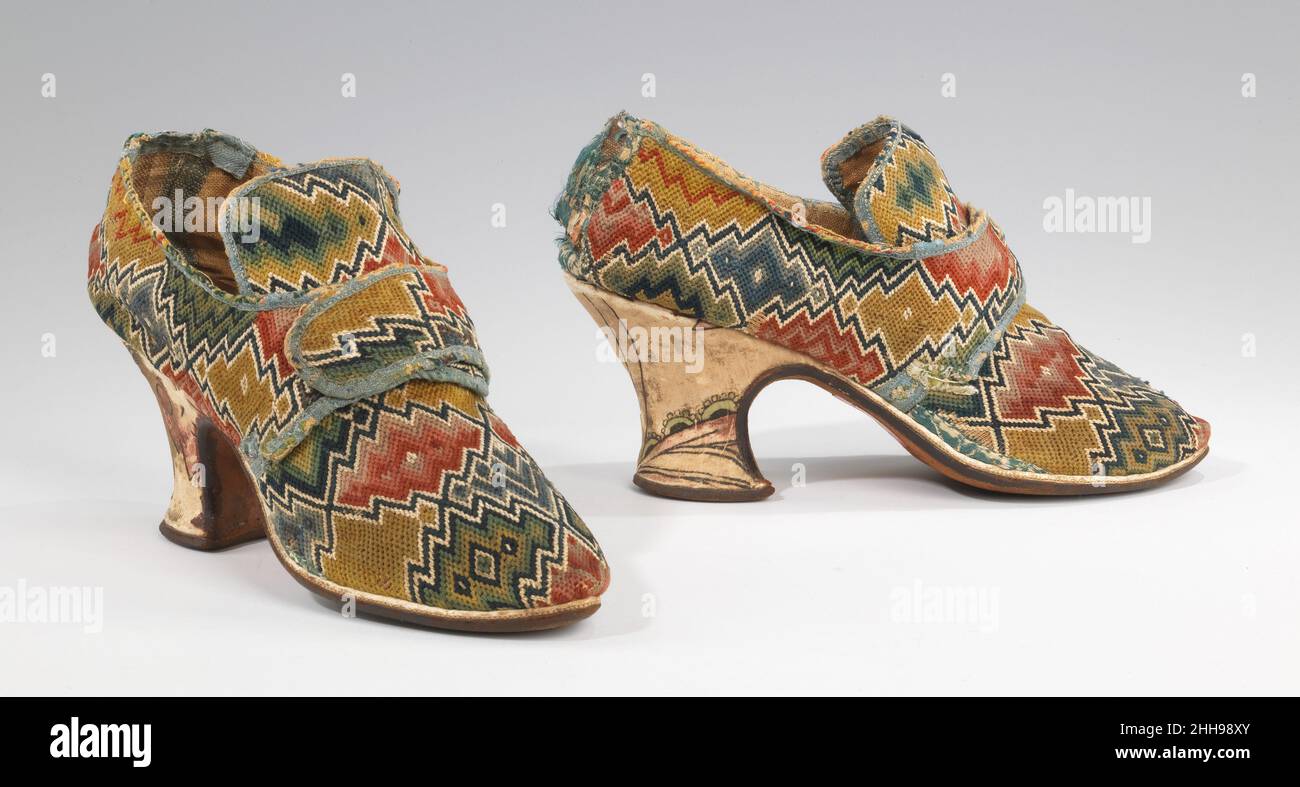 Scarpe 1750–69 inglesi la tomaia con cuciture a fiamma, molto audace, colorata e finemente lavorata, è subito un punto d'occhio su questo paio di scarpe a latchet. Un comune stile di ricamo, il lavoro di tela con punto a fiamma è conservato in molti esemplari del periodo, anche se questo esempio ha un livello inusuale di varietà nel disegno. L'evoluzione della silhouette alla moda si può vedere in confronto ad un altro paio di scarpe con cuciture a fiamma della collezione (2009.300.1411a, b). In questo esempio successivo, possiamo notare il tallone più alto e più verticale, la punta più smussata e meno rovesciata, la suola più piatta e la parte inferiore Foto Stock