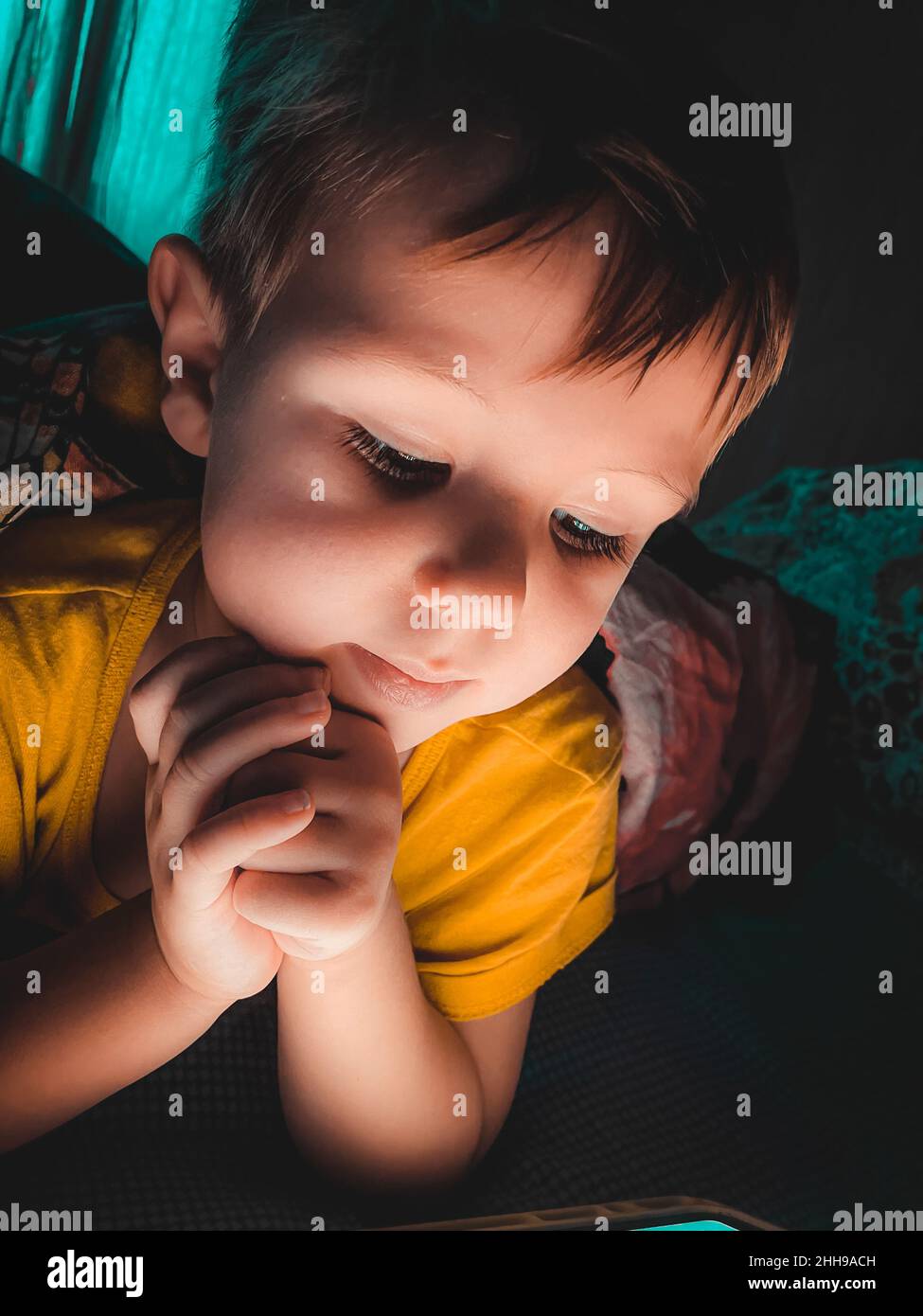 Piccolo ragazzo caucasico che guarda un tablet la sera al buio sul letto, fotografia stile di vita a casa Foto Stock