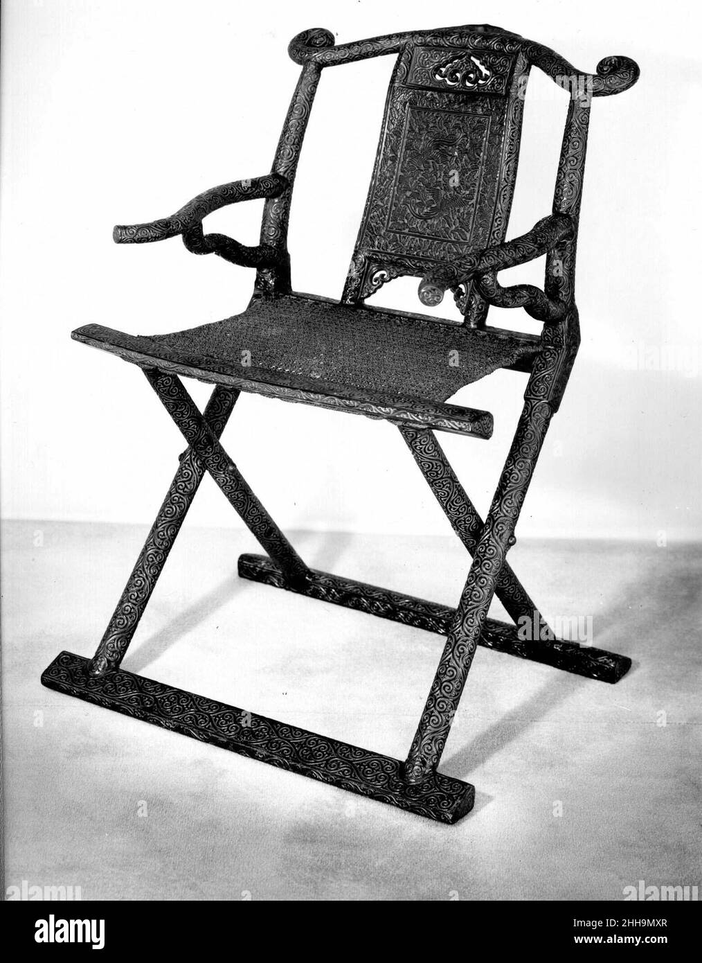 Sedia pieghevole con due uccelli tra i fiori 13th–14th secolo Cina Un esempio molto raro dalla dinastia Ming precoce, questa sedia illustra la sofisticata lavorazione artigianale della lacca e dei mobili del periodo. Le gambe pieghevoli sono ben bilanciate con i braccioli e la schiena ricurva, che insieme creano una struttura stabile e bella. Ad eccezione del sedile in rattan, tutte le superfici della sedia sono in lacca. Oltre allo sfondo geometrico meticolosamente intagliato, la sedia presenta anche un paio di flycatcher paradiso tra i fiori sul pannello posteriore. Noto come "nastro di premiazione" (sh Foto Stock