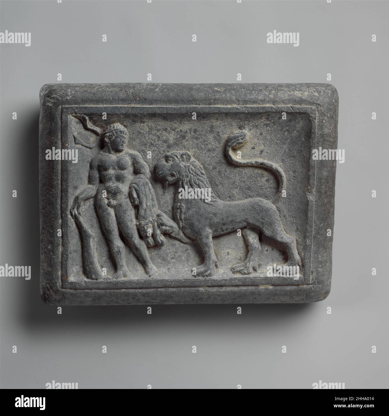 Il peso del lottatore con Ercole e il Leone Nemeo; scena del wrestling (reverse) ca. 1st secolo Pakistan (regione antica di Gandhara) come la prima delle sue dodici fatiche, l'eroe mitico greco Herakles fu ordinato di uccidere il mostruoso leone Nemeo. Poiché la pelle della bestia era impermeabile alle lance e alle frecce, Herakles lo strangolò. Poi Skinned il leone, prendendo il bacino come un mantello e la testa come un casco. La pelle del leone ardesia sul braccio sinistro suggerisce che la figura su questo peso è Herakles, anche se non ci è spiegazione evidente per il leone zoppicante che lo accompagna. Due metà- Foto Stock