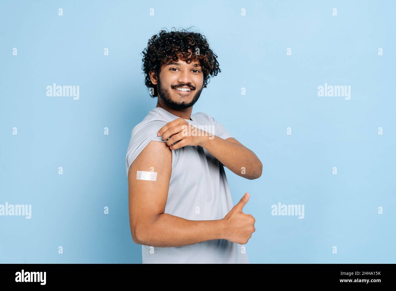 Concetto di assistenza sanitaria, trattamento, prevenzione, vaccinazione. Vaccinazione durante il coronavirus covid 19 pandemia e influenza. Ragazzo indiano con aiuto banda sulla spalla dopo la vaccinazione, sfondo blu isolato Foto Stock