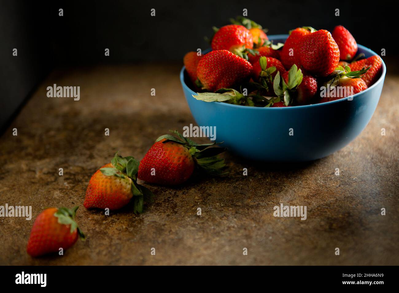 Una ciotola blu di fragole fresche con illuminazione scura e soffusa Foto Stock