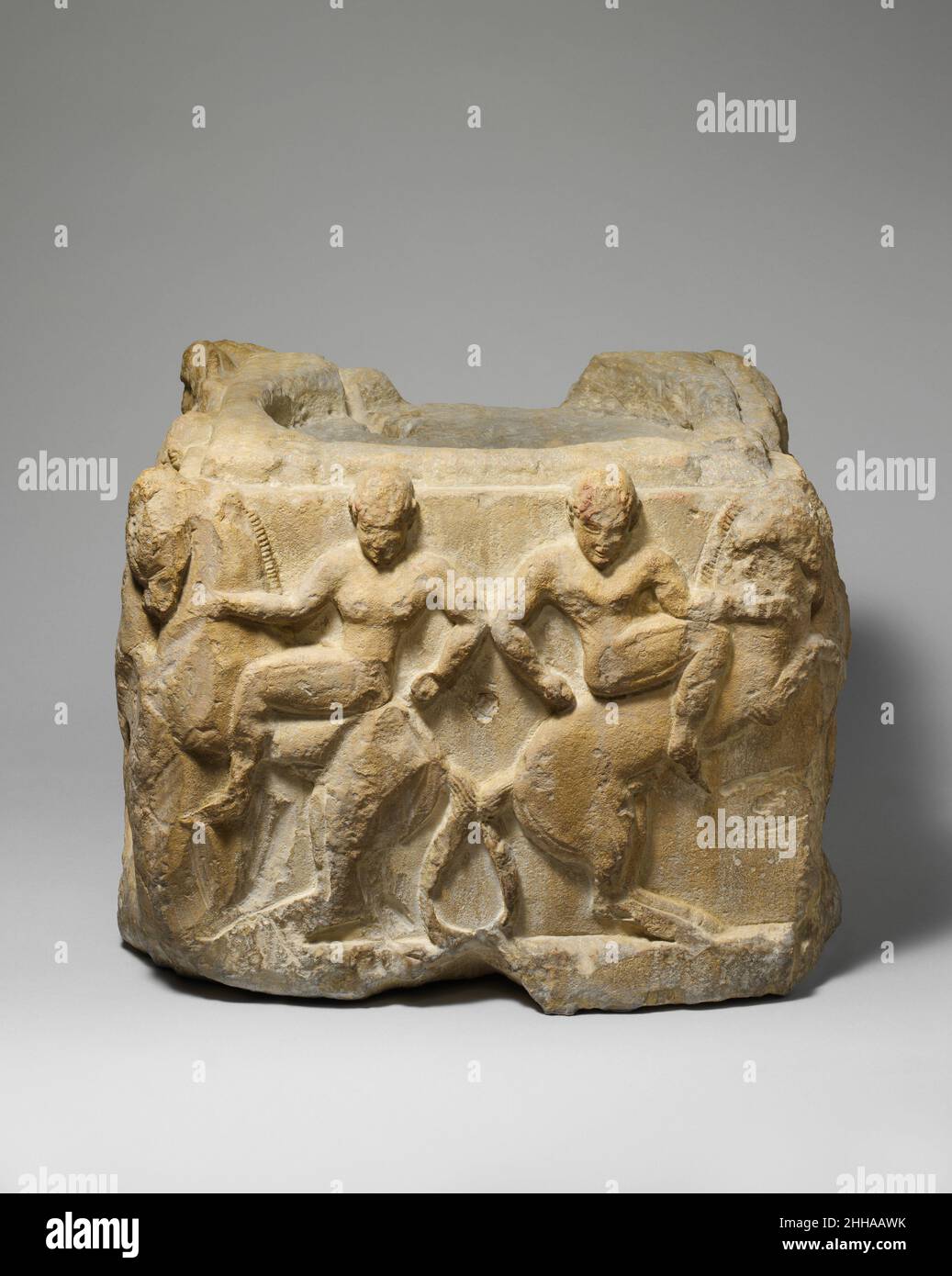 Base di cippus calcarei ca. 500–450 a.C. Etrusco, probabilmente Chiusine A cippus è un grande marcatore in pietra utilizzato dagli Etruschi per stabilire un confine o, più comunemente, per segnare la posizione di una tomba. Gli Etruschi producevano diversi tipi di cippi. Questo esempio, l'unico nella collezione del Museo, è un blocco cubico che in origine avrebbe sostenuto una pietra sferica grande, a forma di cipolla, o appuntita. Ogni lato del blocco è scolpito con una scena identica che mostra cavalieri disposti simmetricamente. Questi quasi certamente rappresentano gli dei gemelli, Castur e Pultucce (romano: Castor e Pollux), amo Foto Stock