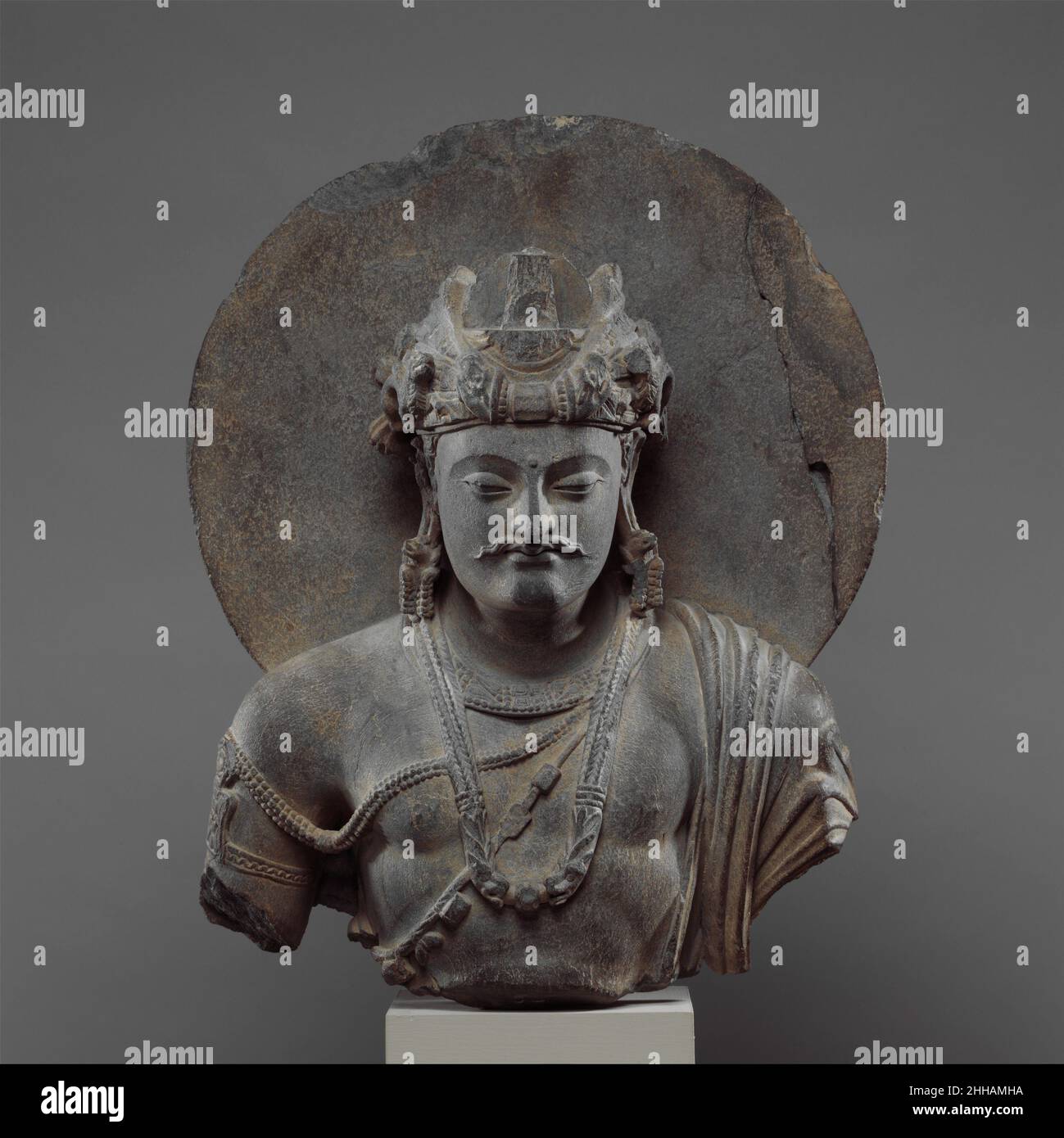 Busto di Bodhisattva Shakyamuni 3rd–4th Pakistan (antica regione di Gandhara) le rappresentazioni di Shakyamuni prima della sua illuminazione come bodhisattva erano popolari a Gandhara, in quanto sottolineano la sua alta rinascita e potenziale per diventare un re chakravartin (monarca universale). Sembra probabile che tali immagini fossero anche destinate a glorificare la grande partenza di Shakyamuni dal palazzo, nel momento in cui lascia il mondo illusorio del desiderio e dell'attaccamento per cercare l'illuminazione. Busto di un Bodhisattva Shakyamuni. Pakistan (regione antica di Gandhara). 3rd–4th secolo. Schist. Scultura Foto Stock