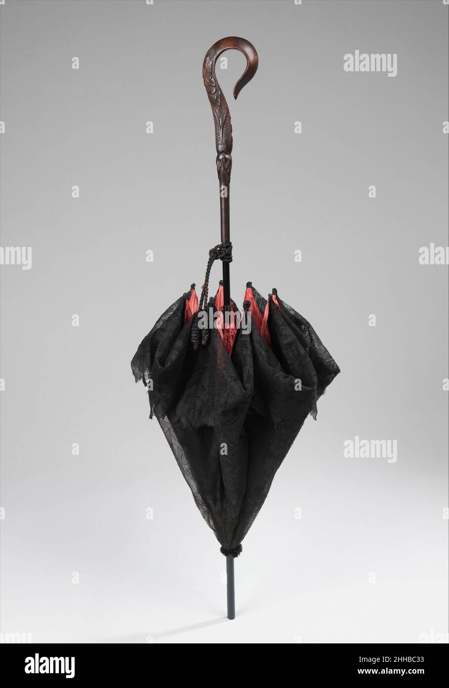 Parasolo 1885–95 probabilmente francese mentre questo parasolo ha un esterno nero semplice, l'interno è una seta changeante in un rosso muto che copre completamente i meccanismi interni. Il manico è particolarmente raffinato nella sua incisione, in quanto il motivo a foglia su un lato è stato scolpito dalla base, dando un aspetto 3D al disegno. Inoltre, la forma del crook è asimmetrica ed elegante. Ombrellone 157912 Foto Stock