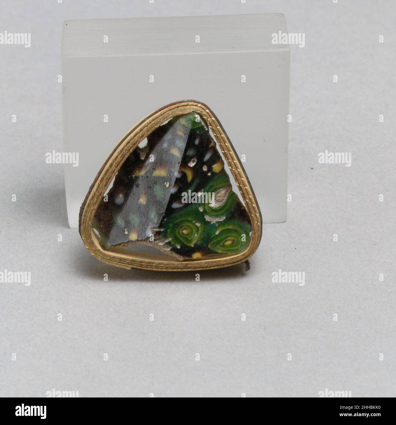 Mosaico di vetro Carinated Bowl fragment fine 1st secolo a.C.–inizio 1st secolo d.C. Roman Body fragment.Translucent Deep purple, turchese apparendo verde, bianco opaco e giallo.lato carinizzato, con parte di due curve convesse, il motivo superiore poco profondo e il motivo inferiore deep.Composite mosaico formato da sezioni poligonali di due canne: Uno in un motivo irregolare di verga verde, gialla e bianca, e l'altro in un blu turchese macinato con una spirale gialla, e un'asta centrale gialla circondata da porpora.lucidato interno; vaiolatura di bolle di superficie su interno; vaiolatura profonda e erbaccia iridescente Foto Stock