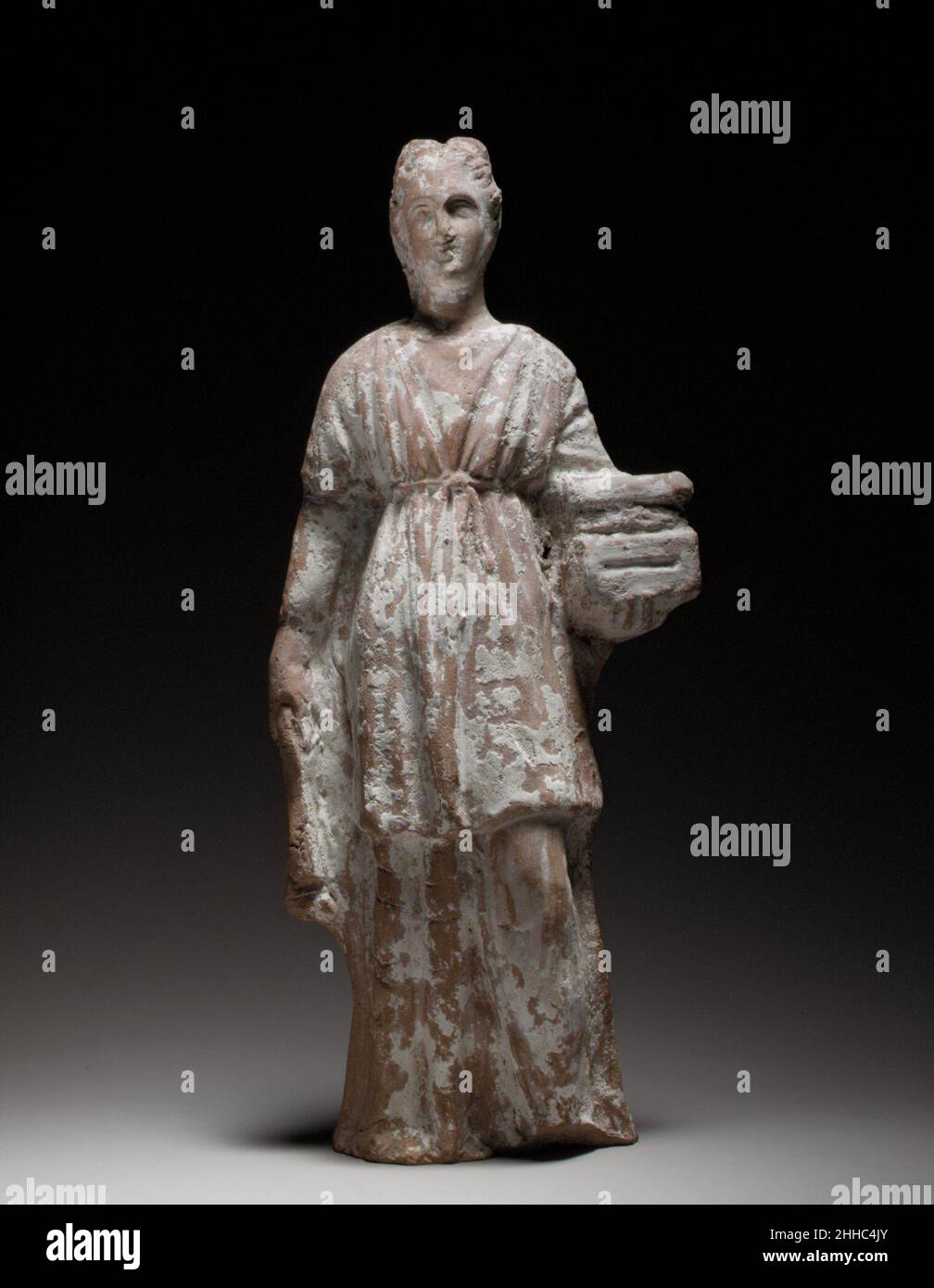 Statuetta in terracotta di una votaria femminile in piedi che detiene una scrigno 3rd–2nd secolo a.C. Cipriota la statuetta è modellata e cava. La schiena è fatta a mano, appiattita e paed. La scrigno che detiene può essere un dono votivo, ma figurine che li portano sono state anche simbolicamente collegate con il matrimonio e la fertilità. Statuina di terracotta di un'votaria femminile in piedi che tiene una cassa 241139 Foto Stock
