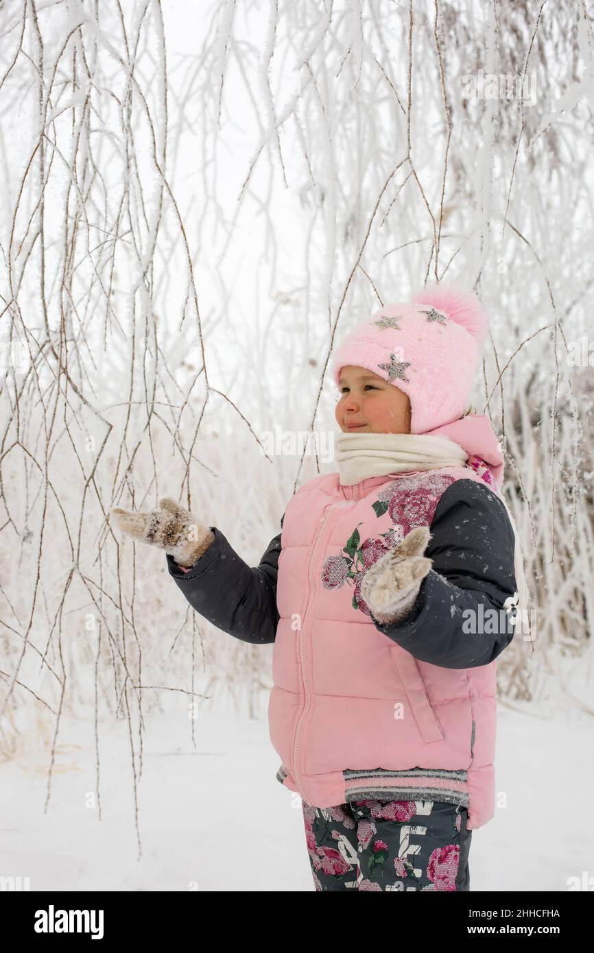 Ragazza donna beatful con guance rosse che guardano i rami dell'albero e che cattura la neve che indossa abiti caldi di inverno con gli alberi innevati sullo sfondo. Passeggiata invernale Foto Stock