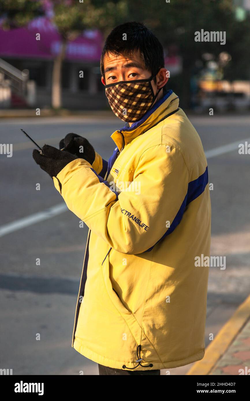 Uomo asiatico indossare maschera e cappotto giallo guardando il fotografo. Jiashan, Cina Foto Stock